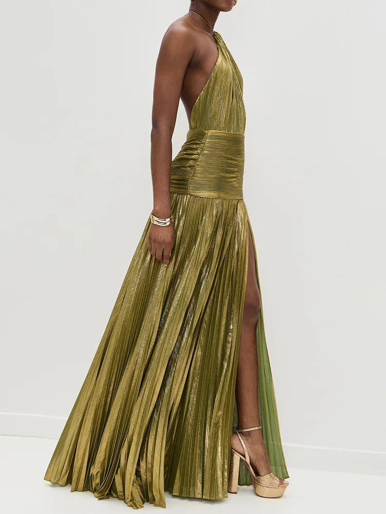 Side profile of model in gold pleated halter maxi dress showcasing the fitted waist, A-line silhouette, and floor-length design
